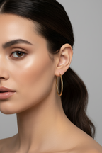 Close-up of a woman wearing gold hoop earrings against a gray background