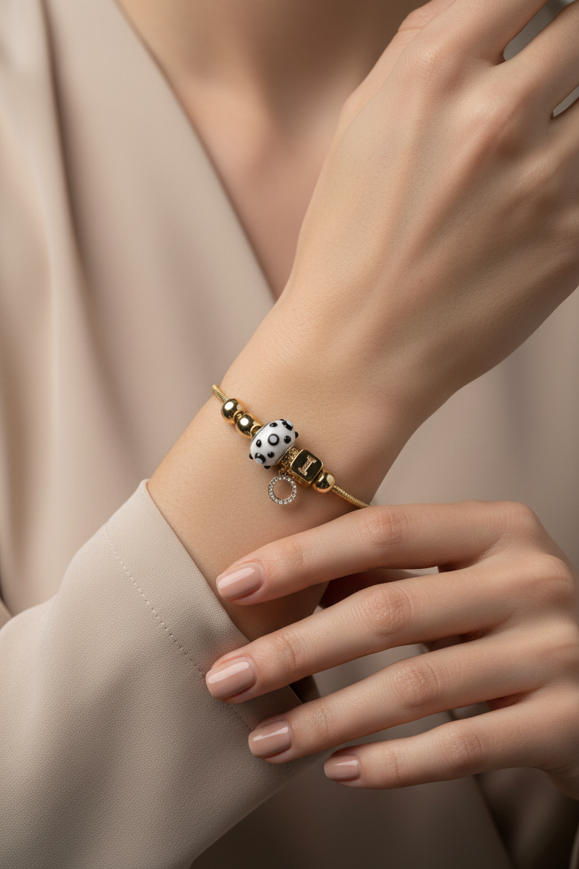 Close-up of a hand wearing a bracelet with a polka dot charm on a neutral background