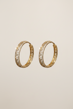 Pair of gold hoop earrings with embedded stones on a beige background