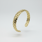 Gold bracelet with textured pattern on a light gray background
