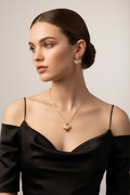 Woman wearing gold heart-shaped necklace and earrings against a neutral background