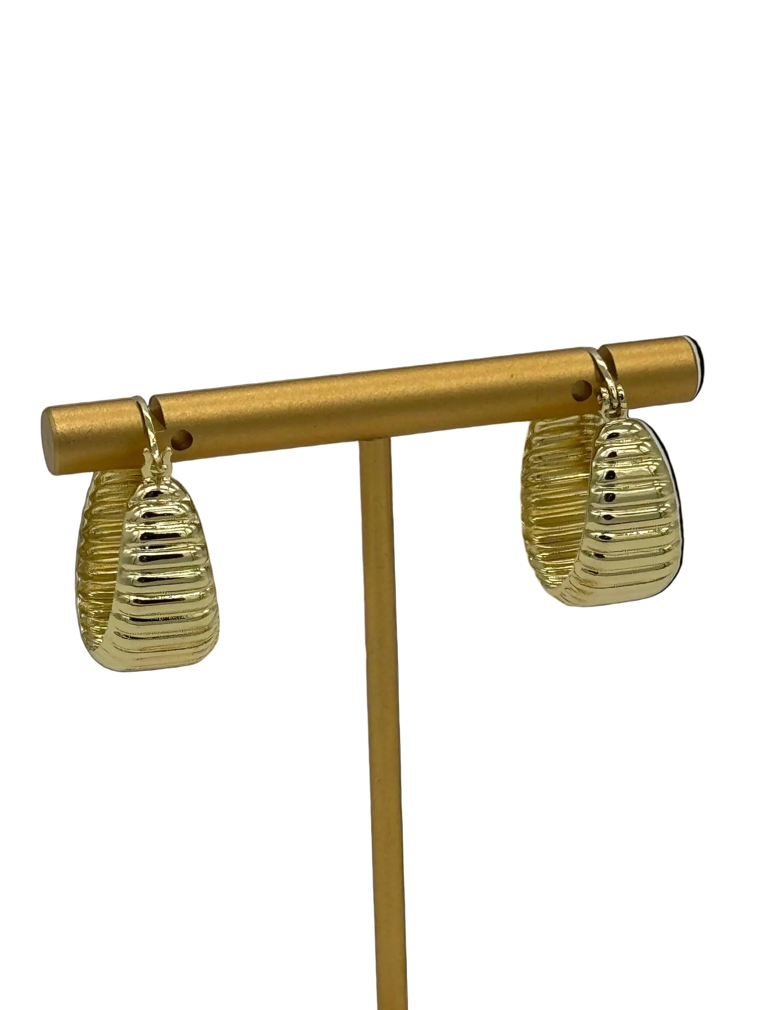 Gold earrings with ribbed design on a light gray background